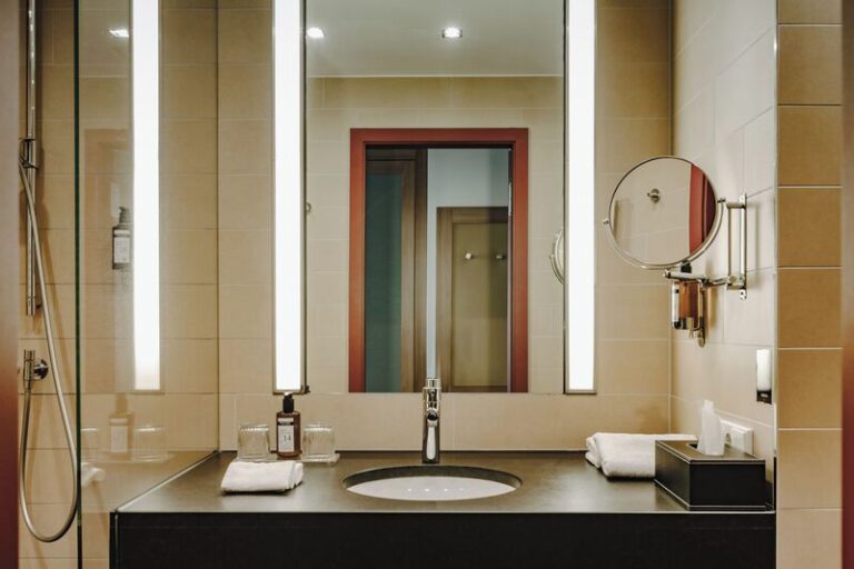 Blick auf ein elegantes Badezimmer mit beleuchtetem Spiegel, Waschbecken, Kosmetikartikeln und hochwertigen Armaturen
