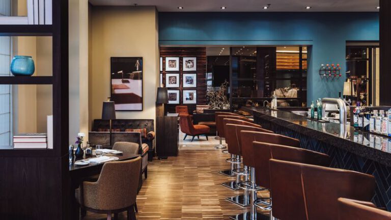 Innenansicht einer eleganten Hotelbar mit Lederbarhockern, modernem Interieur und einem offenen Blick in den Loungebereich