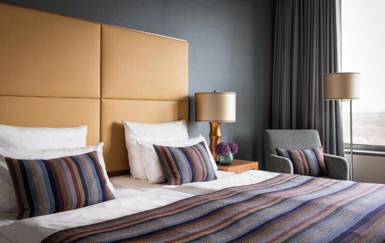 Geräumiges Zimmer mit großem Doppelbett, dekorativen Kissen und stilvollen Nachttischen – Teil des AMERON Köln Hotel Regent